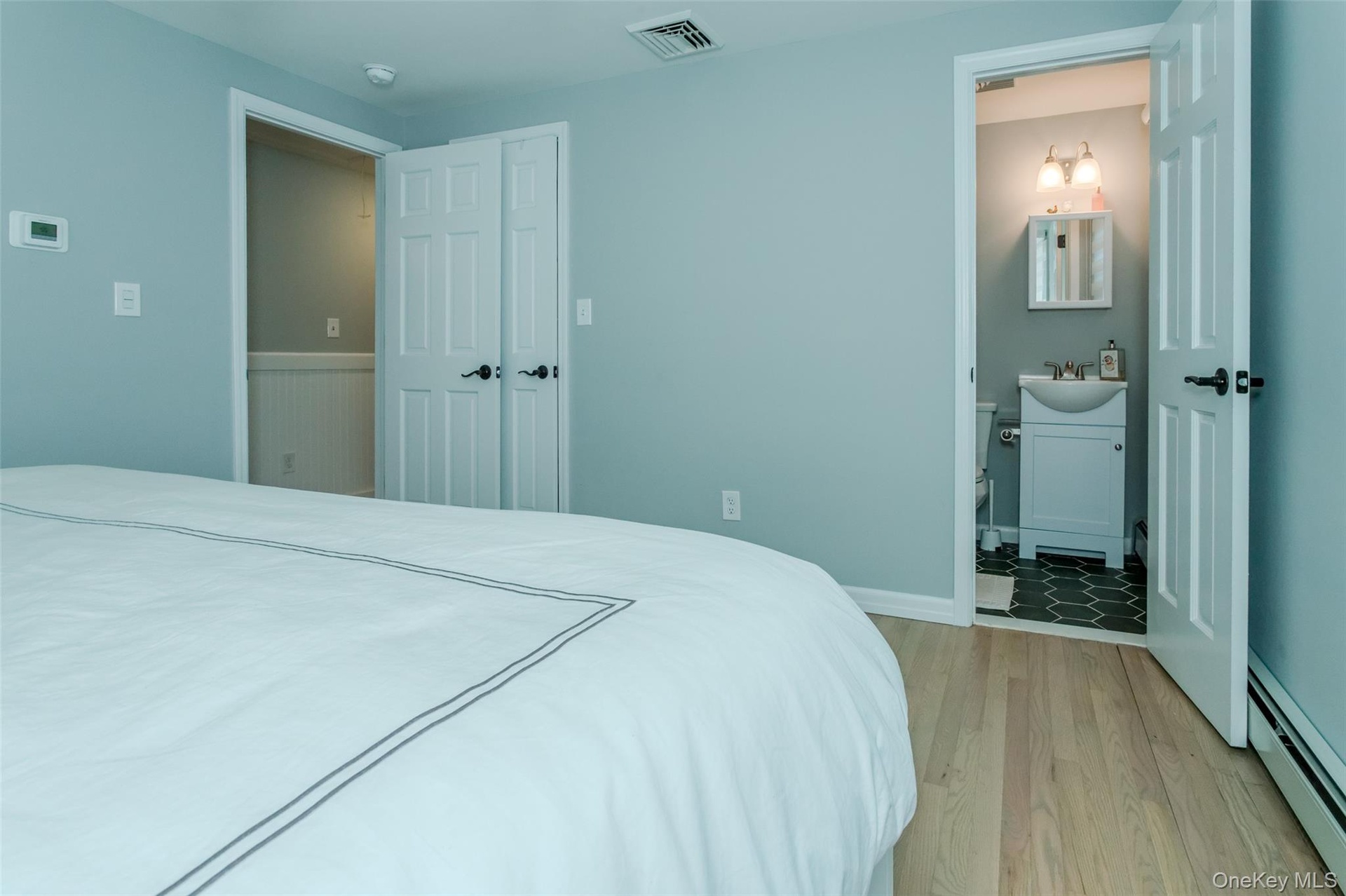 Bedroom featuring connected bathroom, light hardwood / wood-style floors, baseboard heating, and sink
