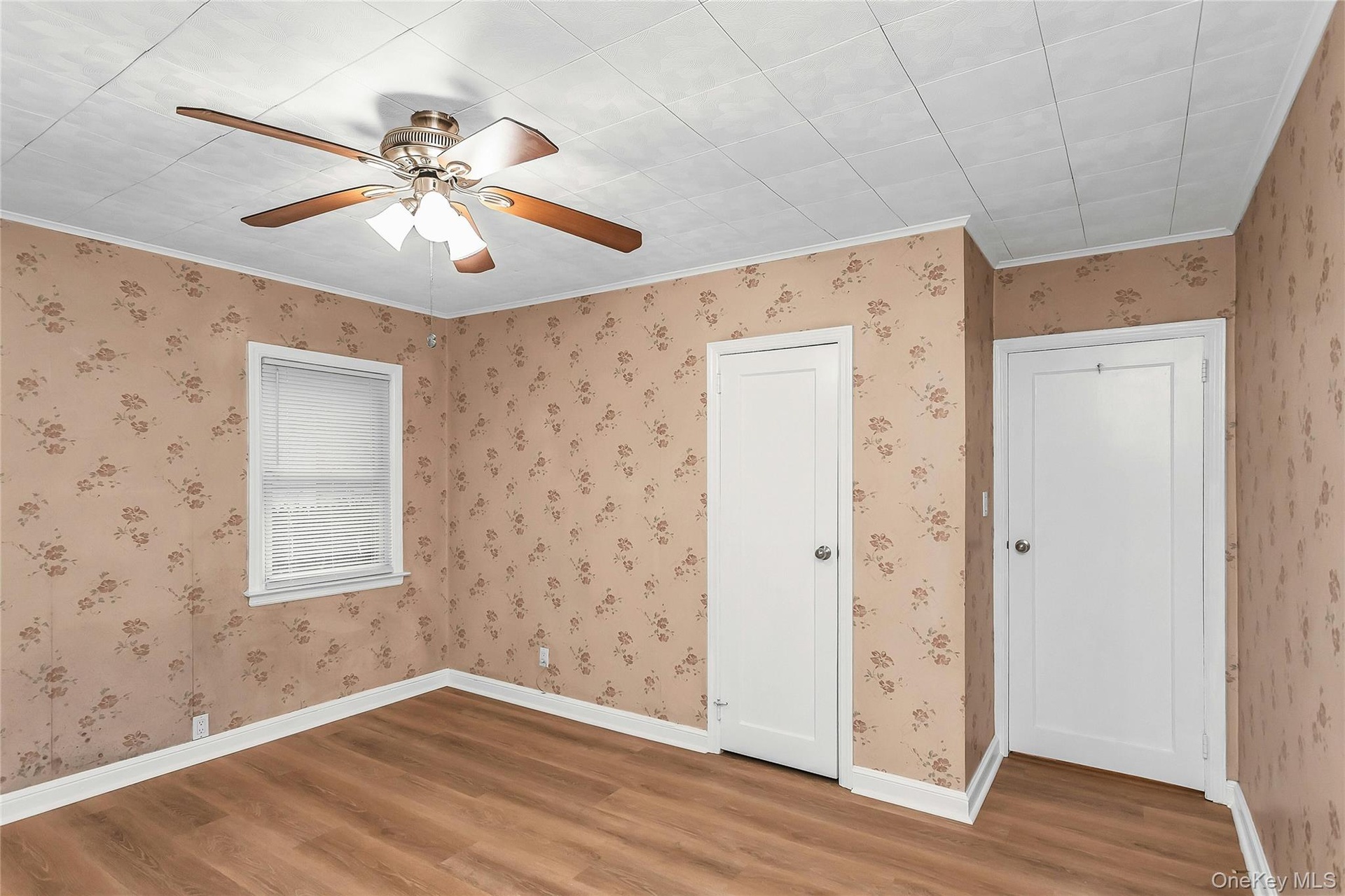 Room featuring wood-finish flooring, a ceiling fan with integrated lighting, and two white panel doors