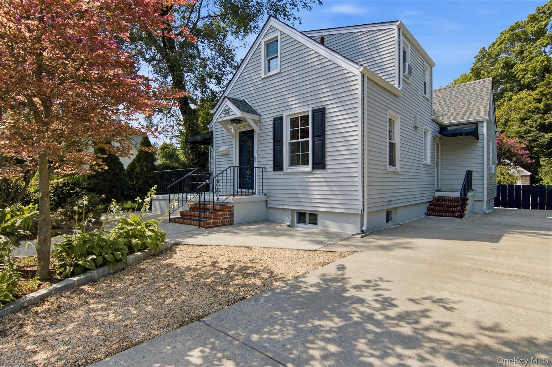 Siding exterior with black window shutters, gabled roofline, brick stairs with black railings, and a concrete driveway