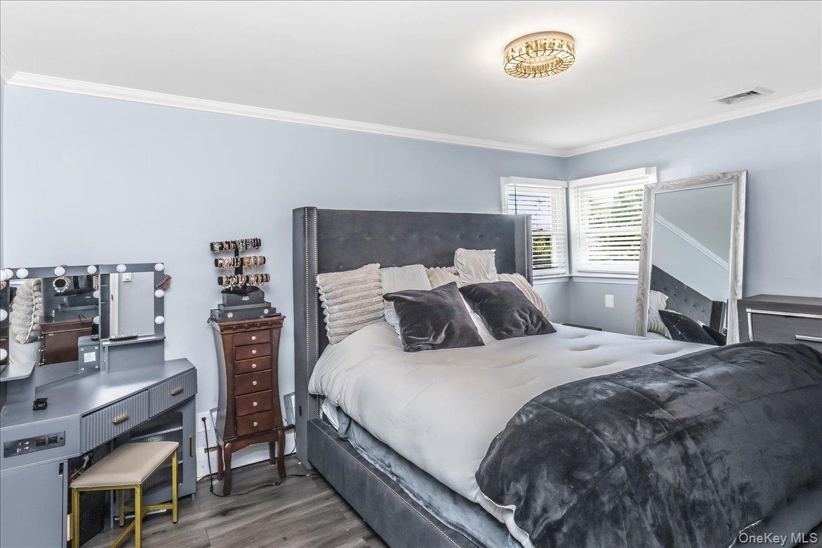 Spacious room featuring light blue walls, crown molding, a decorative flush-mount ceiling fixture, two windows with blinds, and wood-finish flooring