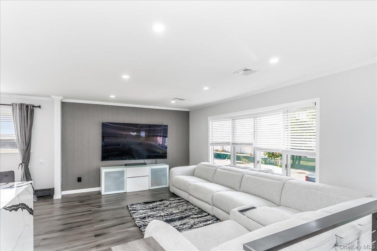Spacious living area featuring wood-finish flooring, recessed lighting, and a prominent accent wall