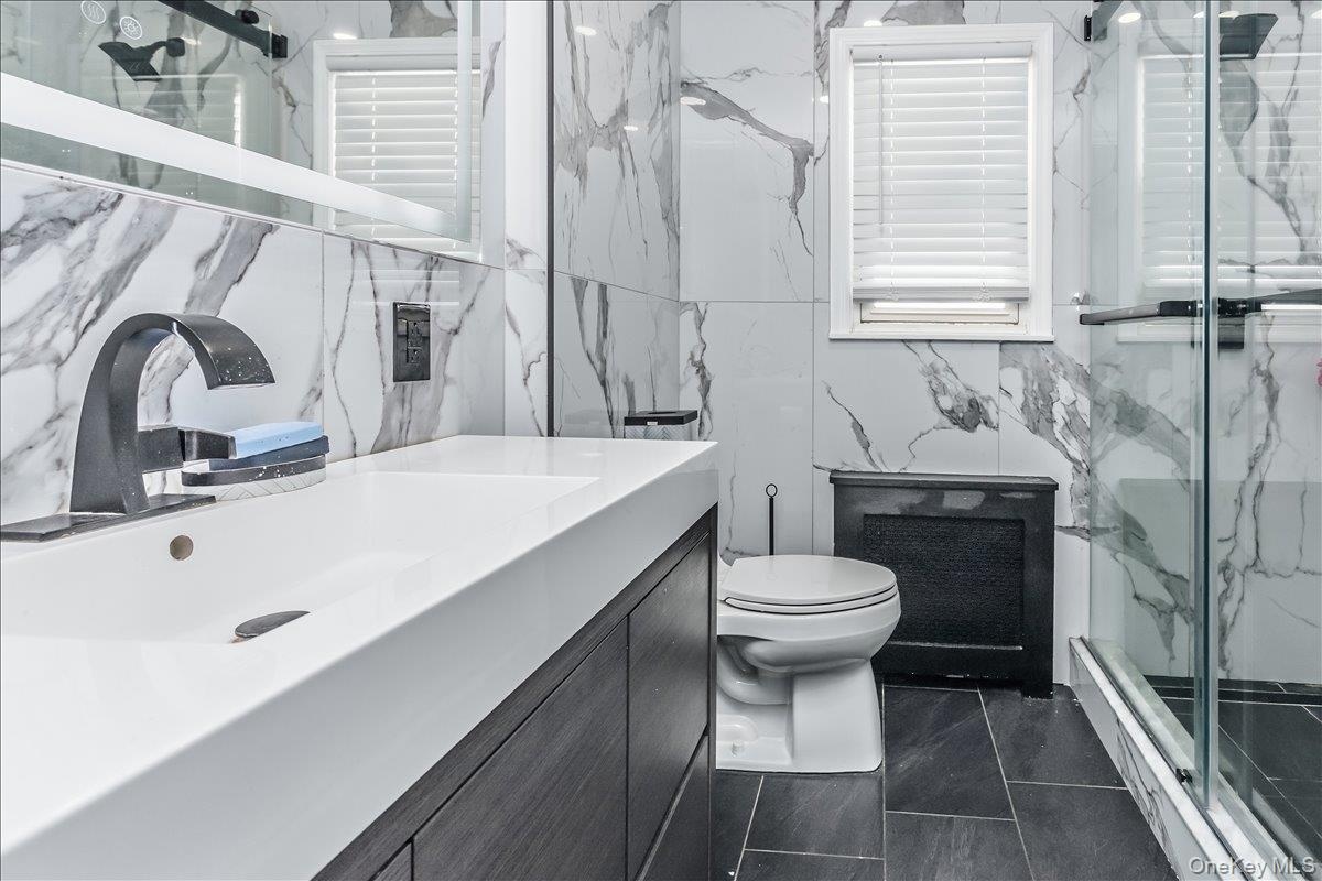 Spa-inspired primary bathroom featuring marble-look wall tile, dark tile flooring, and a floating vanity with an integrated rectangular sink