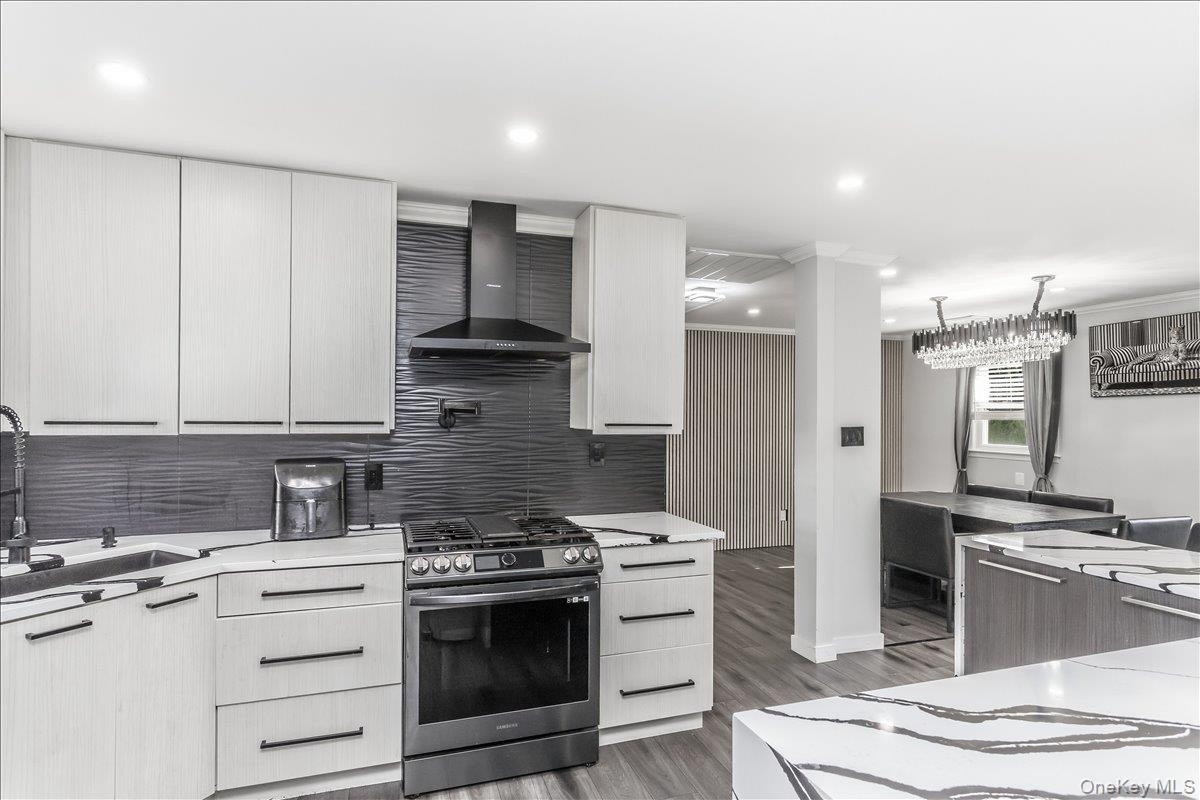 Modern kitchen featuring light wood-finish cabinetry, dark horizontal hardware, and a stainless steel gas range with a coordinating range hood