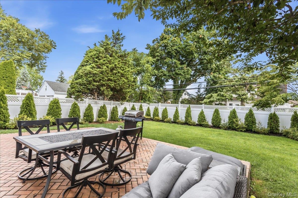 Expansive backyard featuring a brick paver patio, lush green lawn, and mature perimeter trees