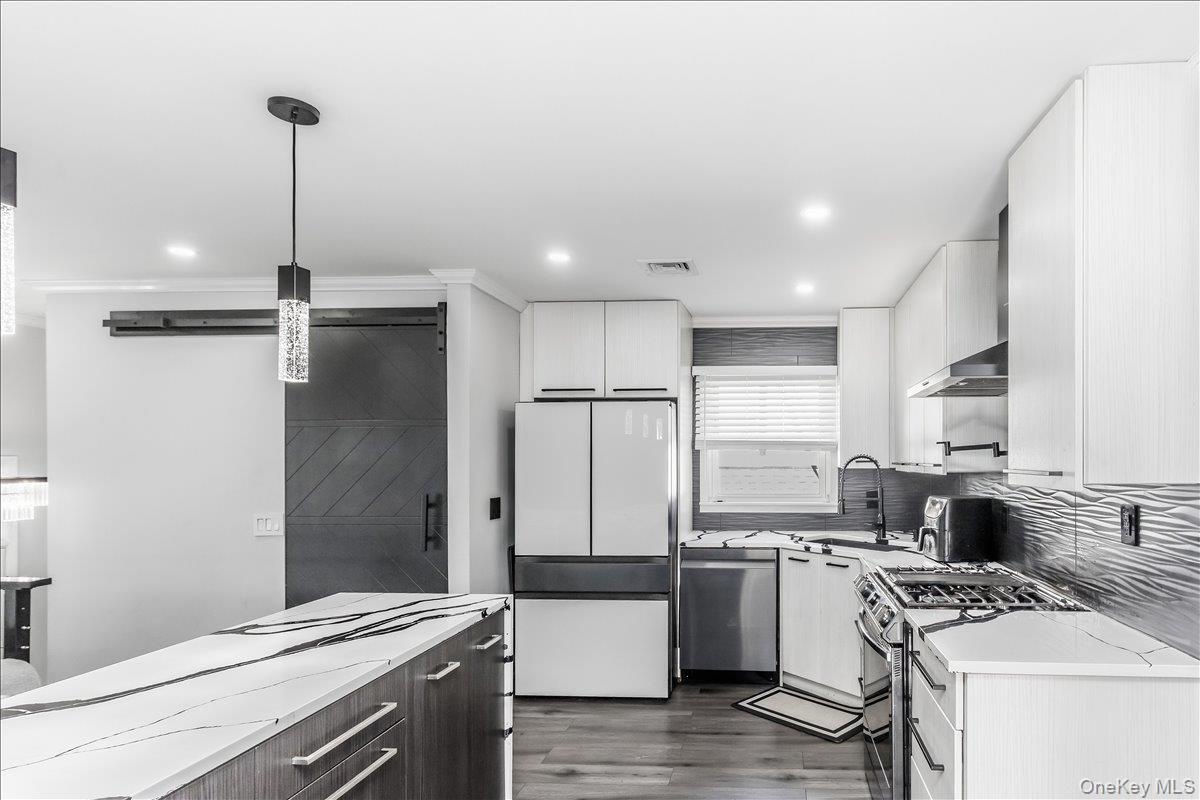 Modern kitchen featuring white cabinetry, a large center island with a white and black veined countertop, stainless steel appliances, wood-finish floo