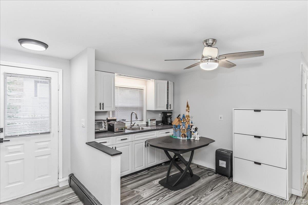 Contemporary kitchen featuring white cabinetry, dark countertops, a stainless steel sink with a gooseneck faucet, and wood-finish flooring