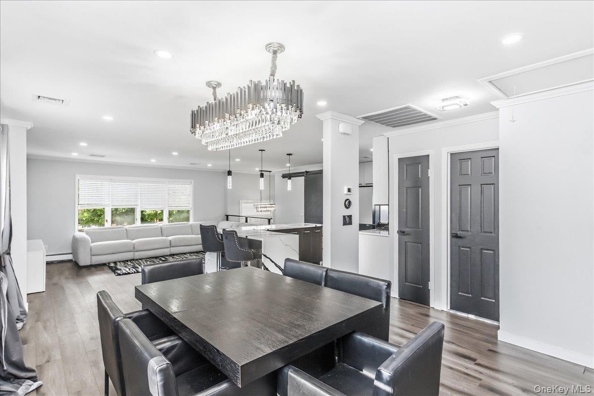 Open-concept interior featuring wood-finish flooring, a contemporary chandelier, recessed lighting, a kitchen island with seating, and dark panel door