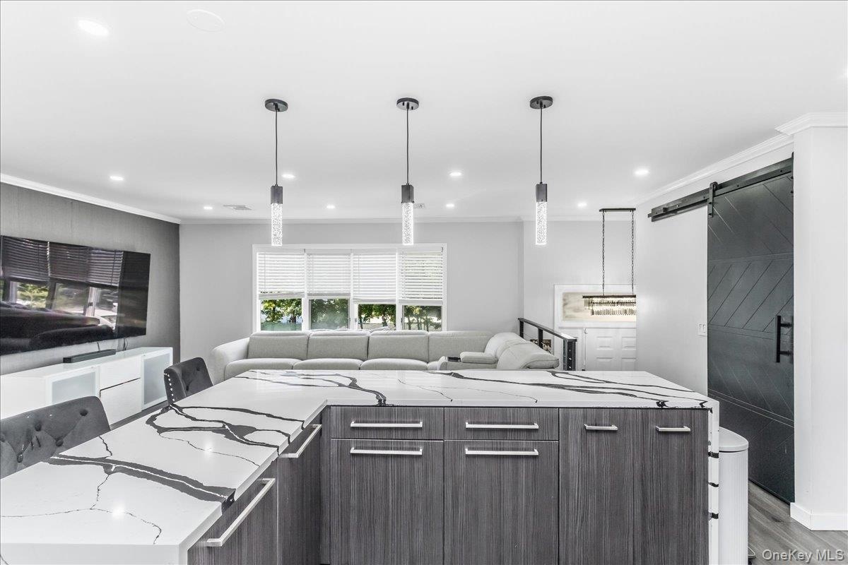 Kitchen island featuring a waterfall-edge countertop with prominent veining, wood-finish cabinetry, and three pendant lights