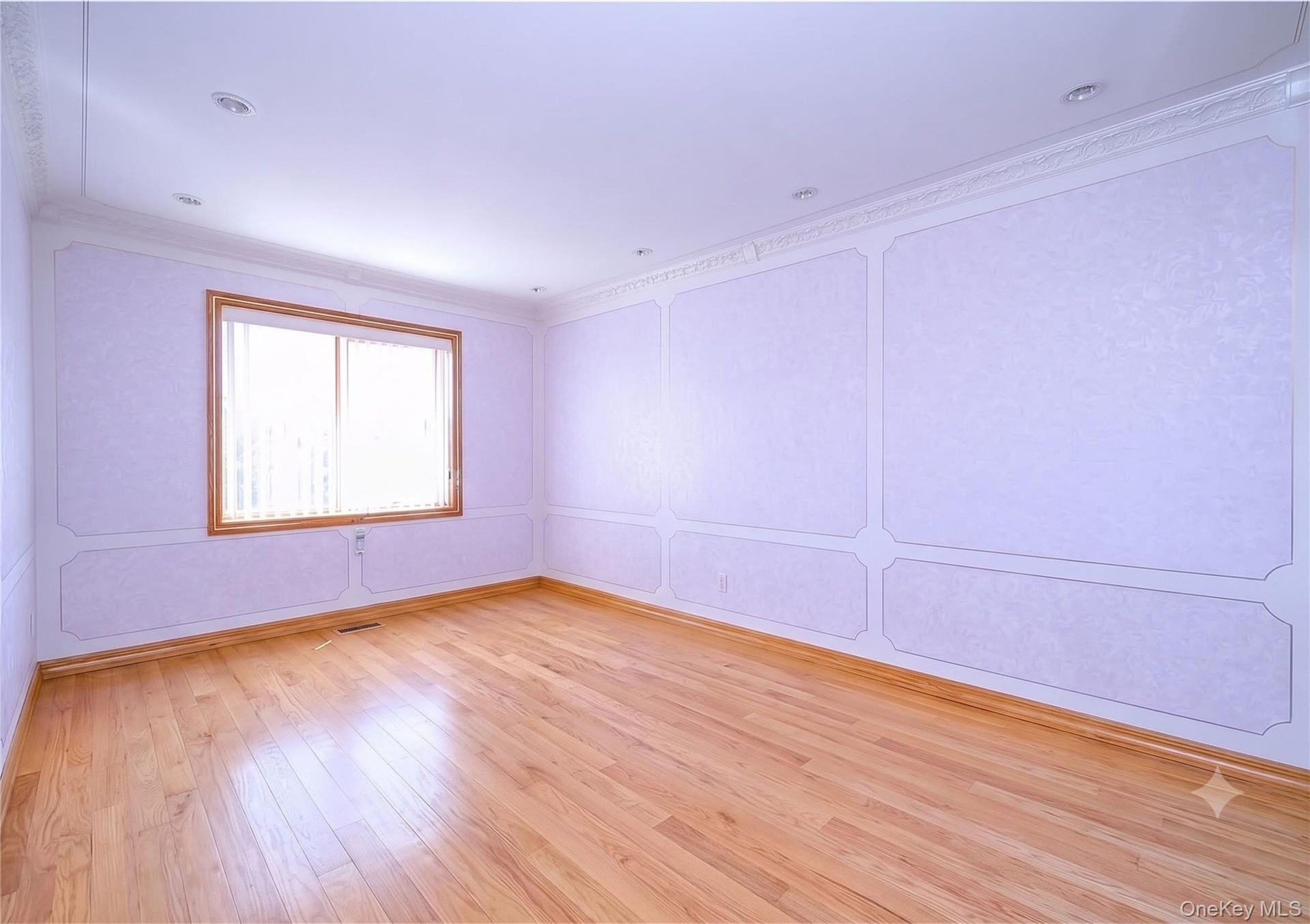 Bright, light-filled room featuring gleaming wood-finish flooring, crisp white wainscoting and wall paneling, recessed ceiling lighting, and a large w