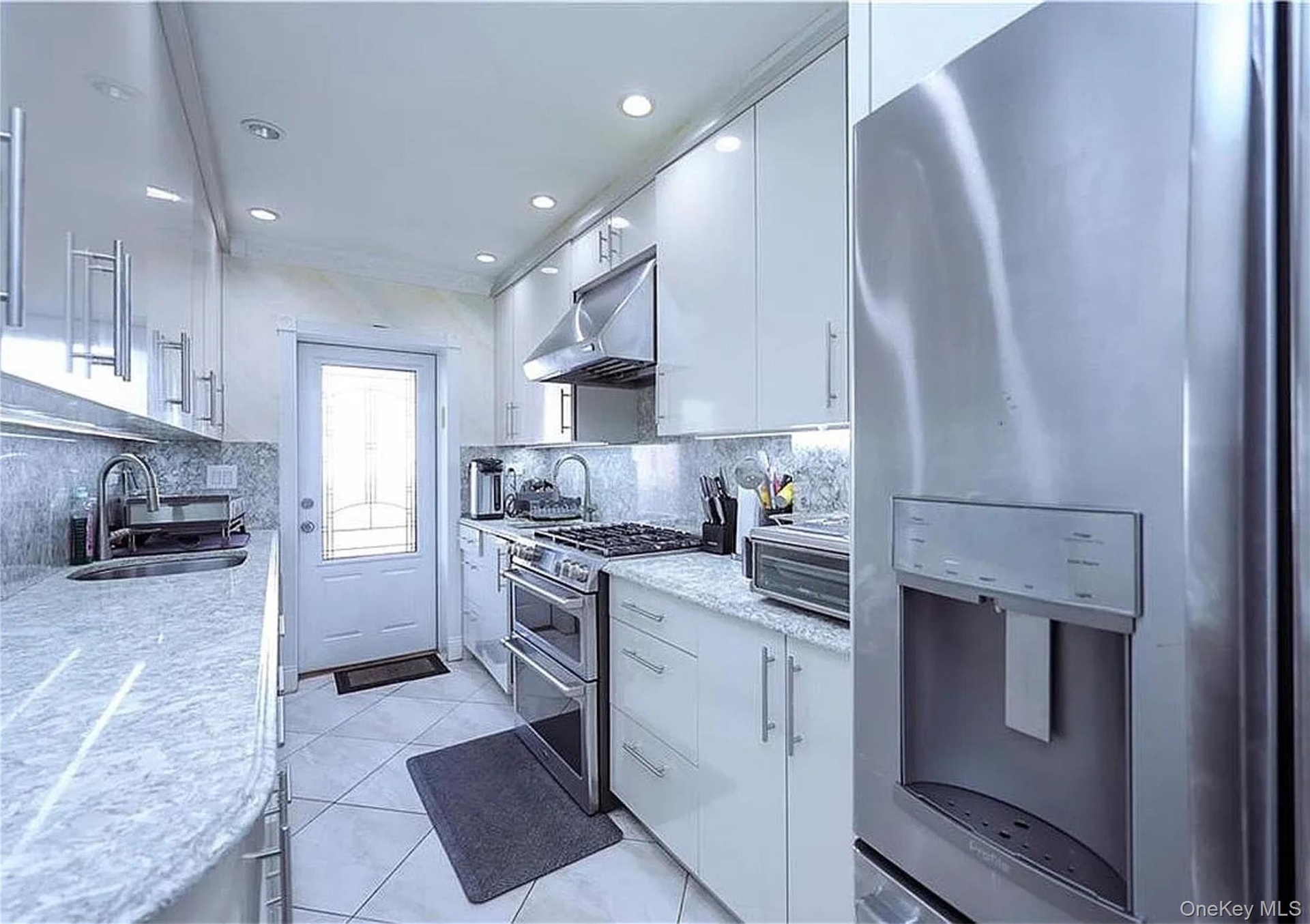Galley kitchen featuring white cabinetry with brushed nickel hardware, granite countertops, stainless steel appliances, and recessed lighting