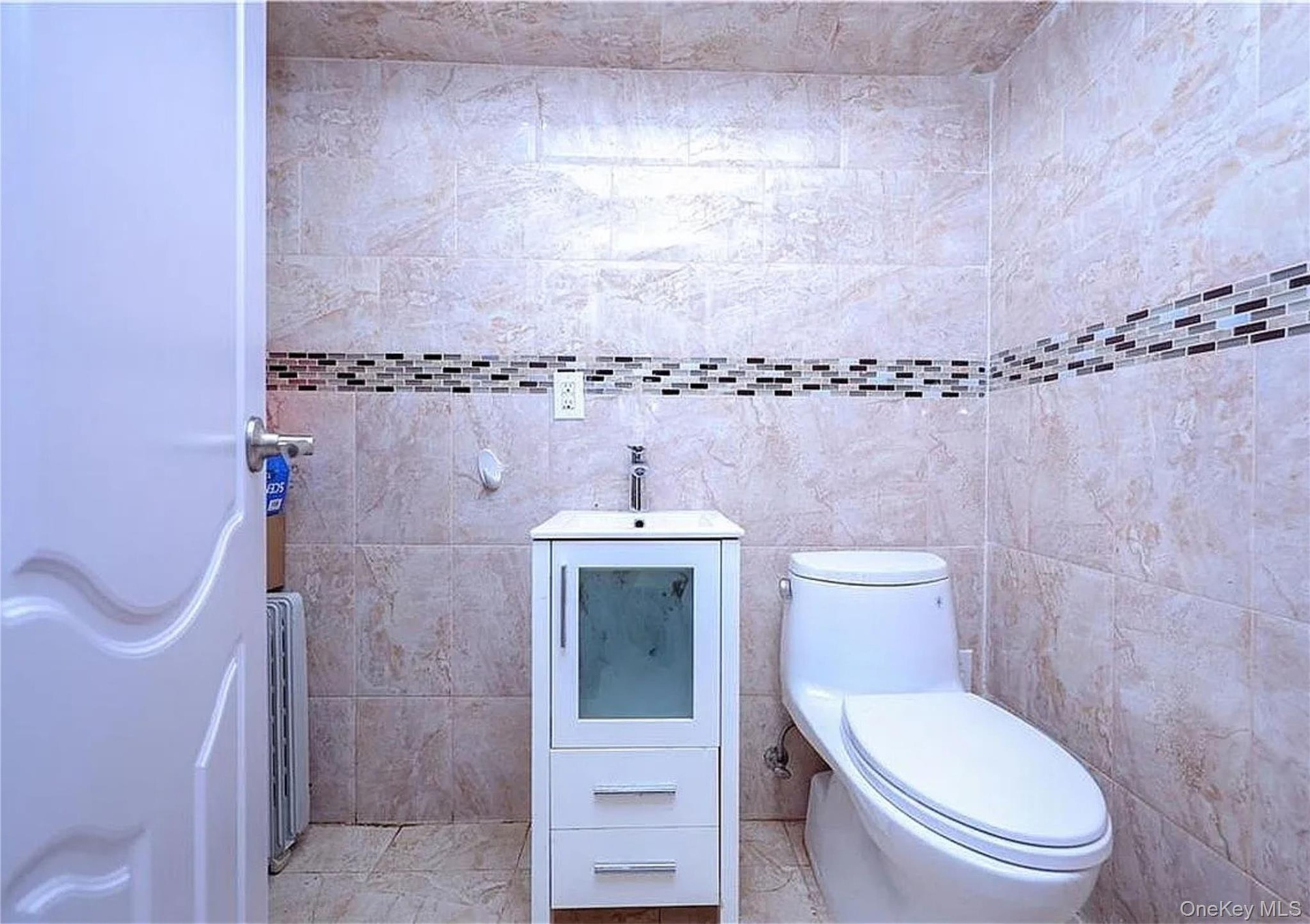Modern bathroom featuring ceramic tile walls with decorative mosaic border stripe, a white vanity with integrated sink and storage drawers, contempora