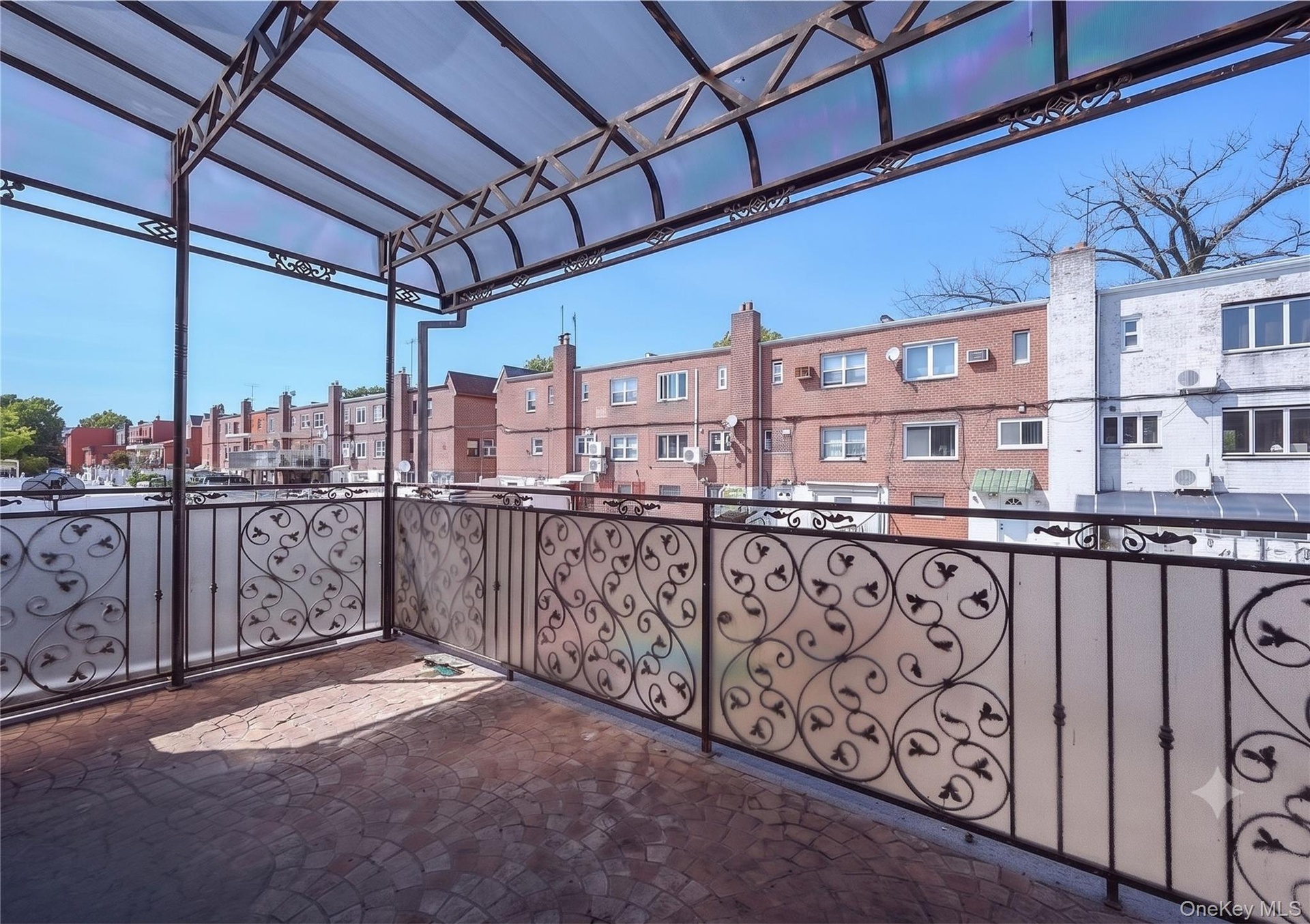 Outdoor patio featuring a clear overhead canopy, decorative metal railings with frosted panels, and brick-patterned paving