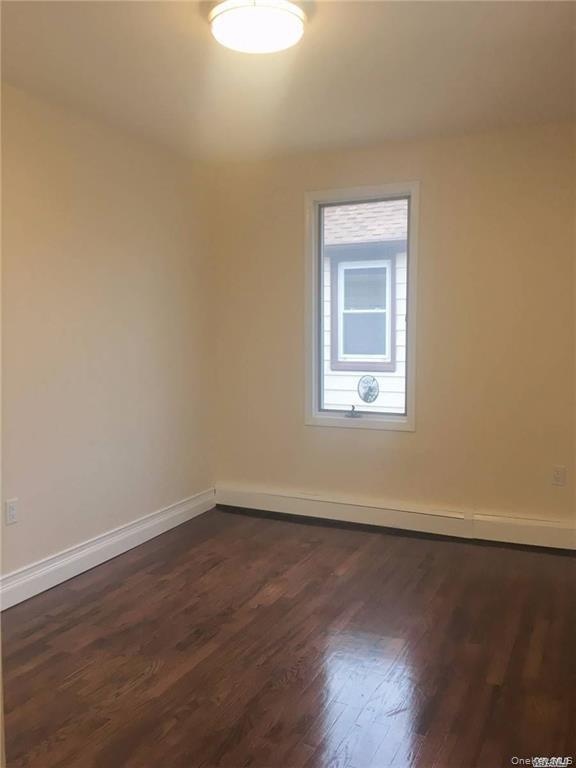 Bright, light-filled bedroom featuring gleaming wood-finish flooring, fresh neutral walls, and a transom window with natural light
