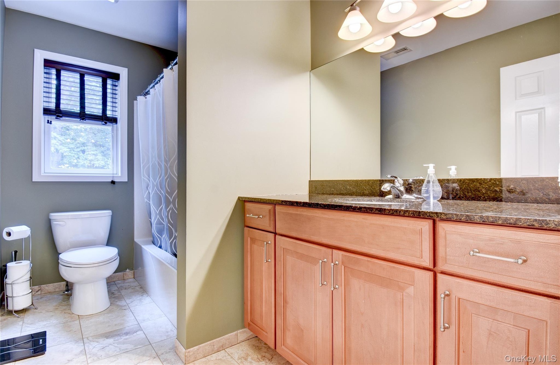 Hall Bathroom featuring a wood-finish vanity with a dark granite countertop and integrated sink, a large wall-mounted mirror, and a sconce light fixtu