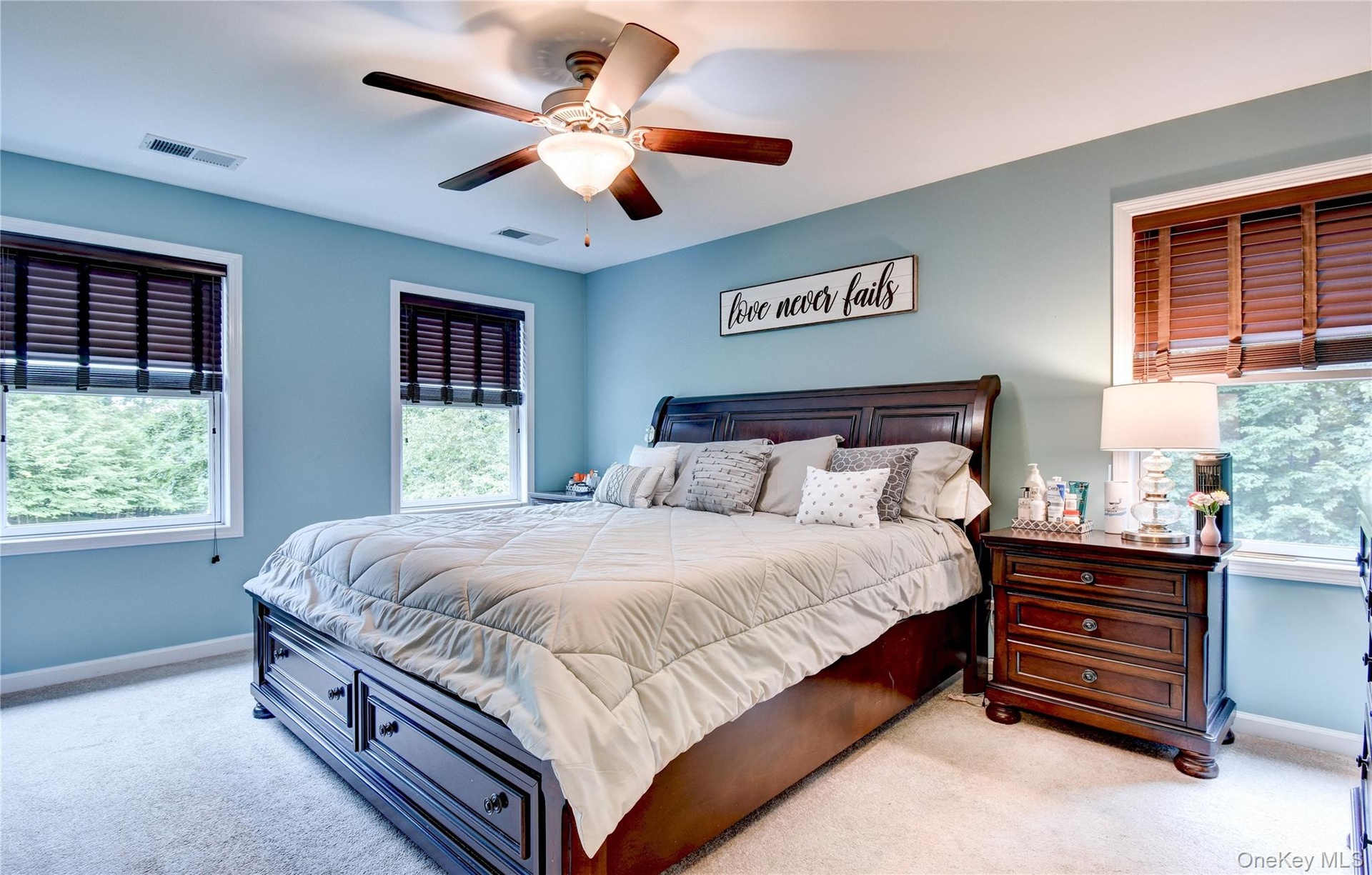 Carpeted primary bedroom featuring a ceiling fan with integrated lighting, two windows with wood slat blinds