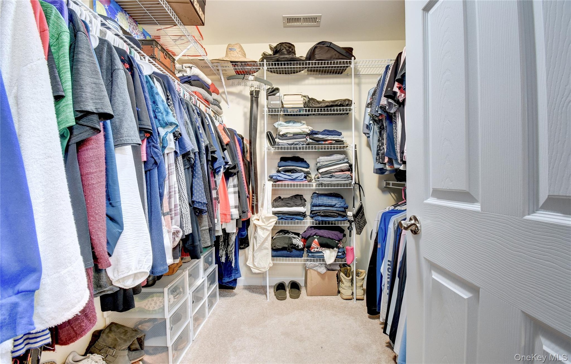 Walk-in closet featuring carpet flooring, white wire shelving, multiple hanging rods, and a paneled door