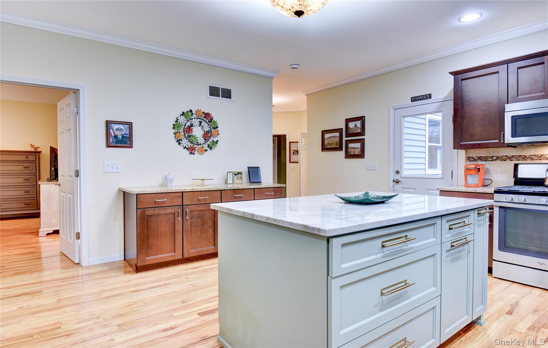 Legal accessory apartment: Kitchen featuring a central island with quartz countertop, light wood flooring, dark wood cabinetry, and stainless steel ap