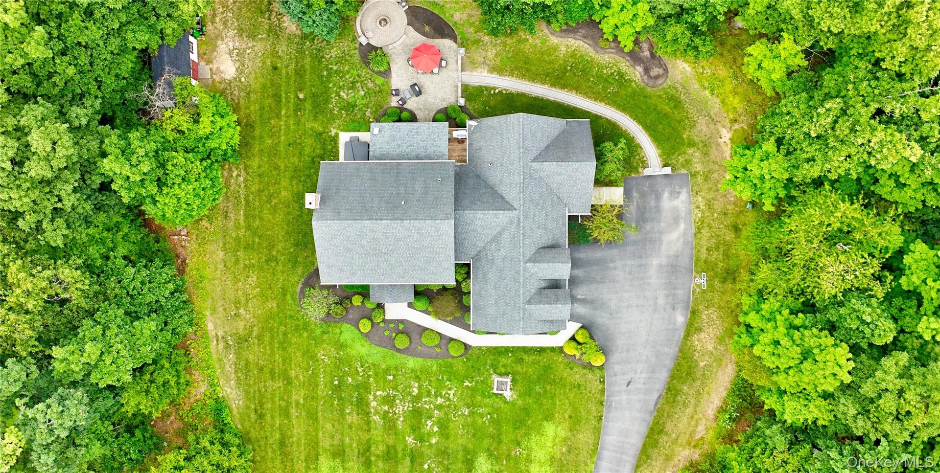 Expansive property featuring a multi-gabled roofline, a paved driveway, and a stone patio