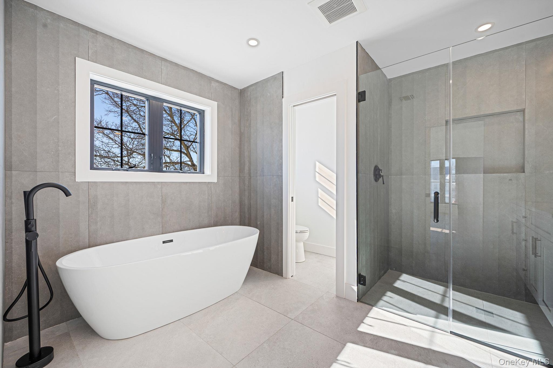 Spa like primary bath featuring a freestanding soaking tub, oversized glass shower, and modern finishes.