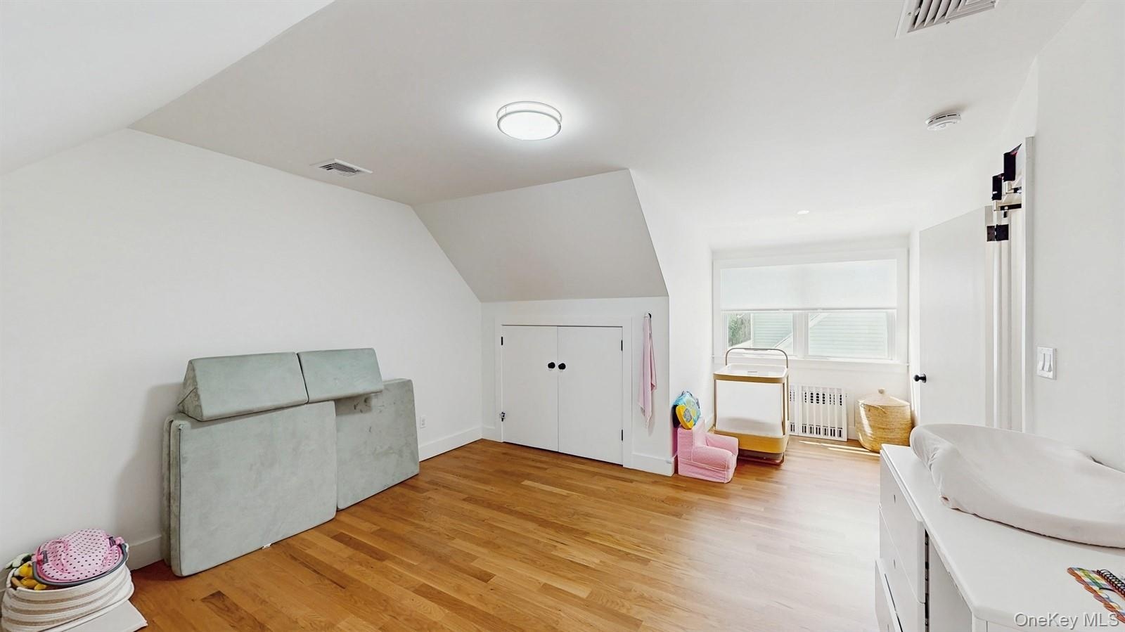 Additional living space with radiator heating unit, visible vents, vaulted ceiling, and light wood-style flooring