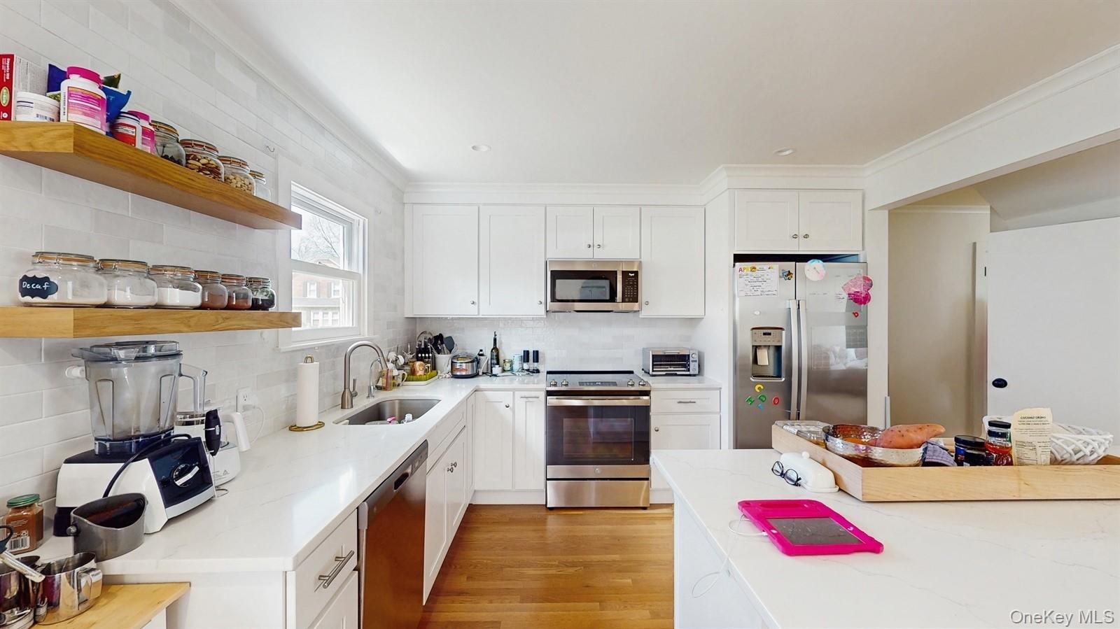 Kitchen featuring tasteful backsplash, open shelves, a sink, stainless steel appliances, and light wood-style flooring