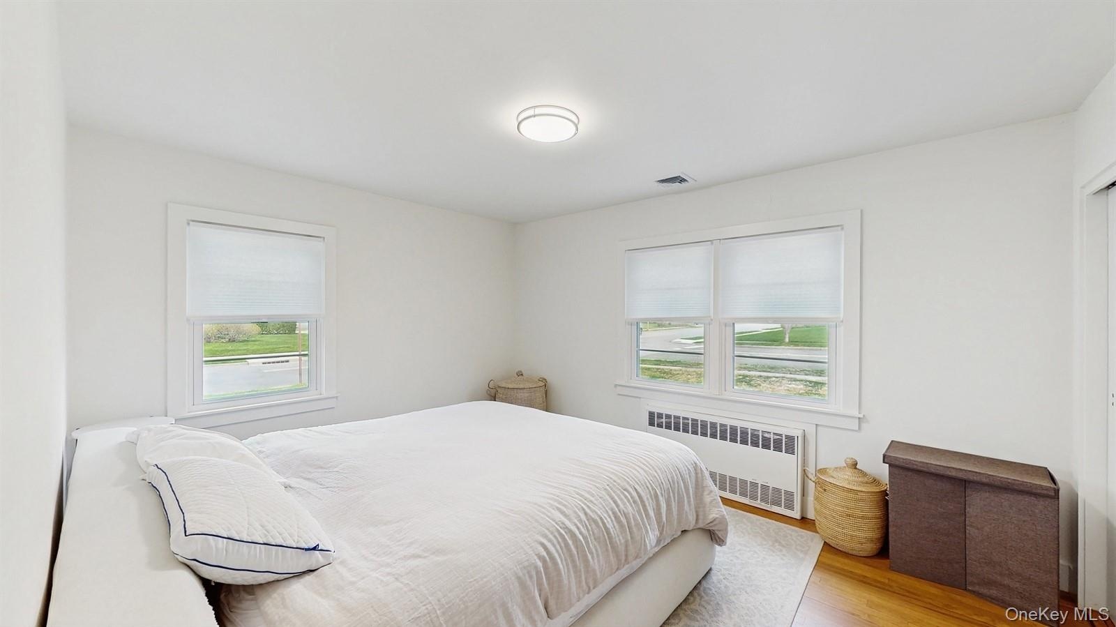 Bedroom featuring visible vents, multiple windows, radiator, and wood finished floors