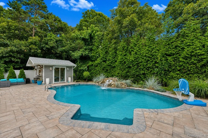 Free-form swimming pool with a rock waterfall feature, complemented by a paver patio surround