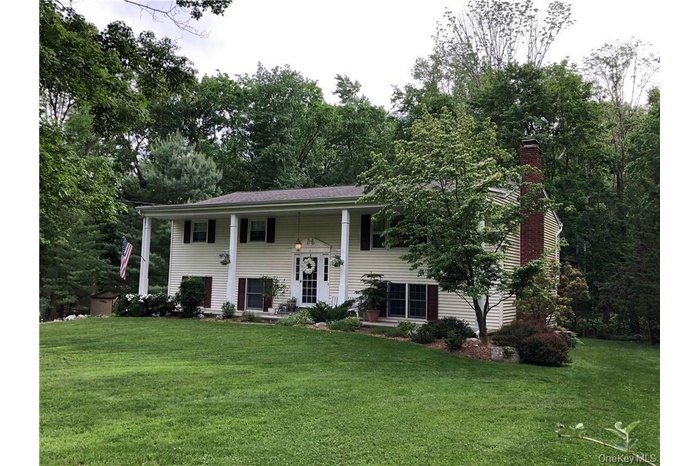 Split-level residence featuring light-colored siding, a covered front porch with white columns, and dark shutters