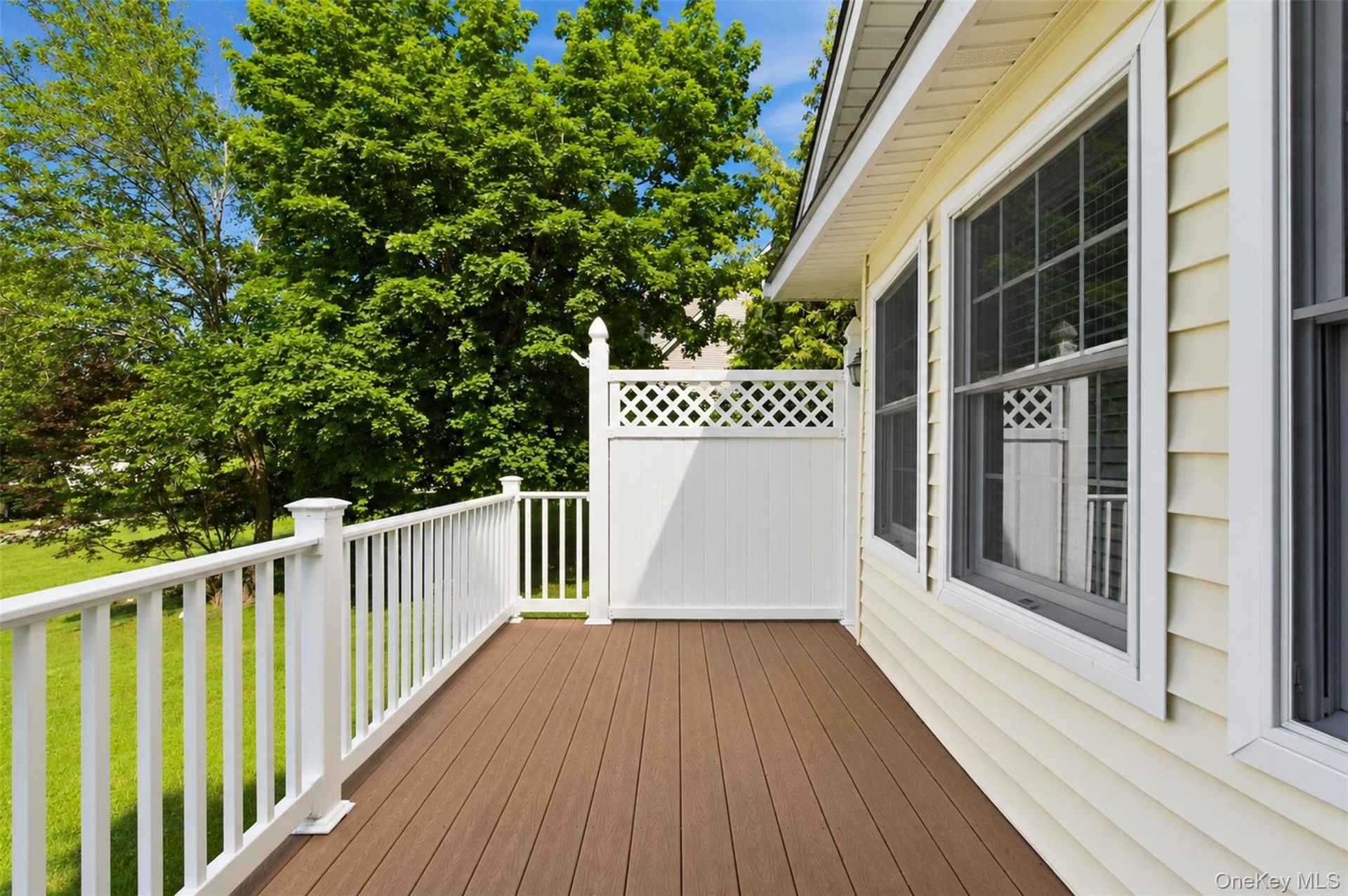 Exterior deck featuring composite wood-finish flooring, white railing, and white lattice privacy screen