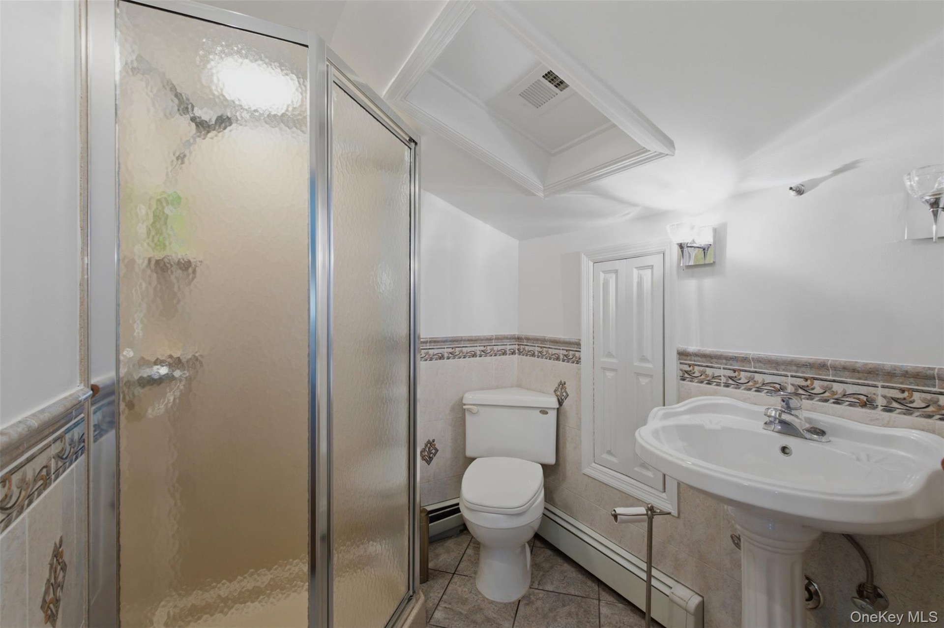 Full Bathroom in 3rd bedroom on the second level featuring a glass-enclosed shower, pedestal sink, ceramic tile flooring, and decorative wainscoting