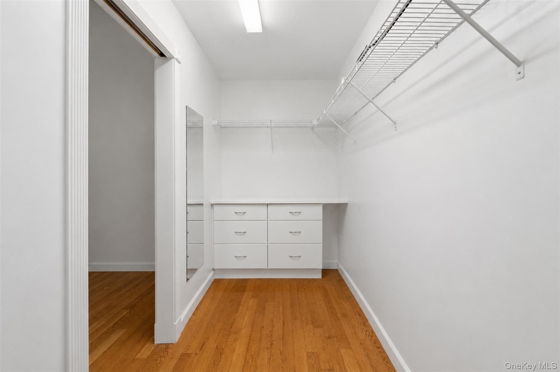 Walk-in closet in bedroom 2 on first level featuring wood-finish flooring, a built-in dresser with six drawers and metal pulls, wire shelving, a full-