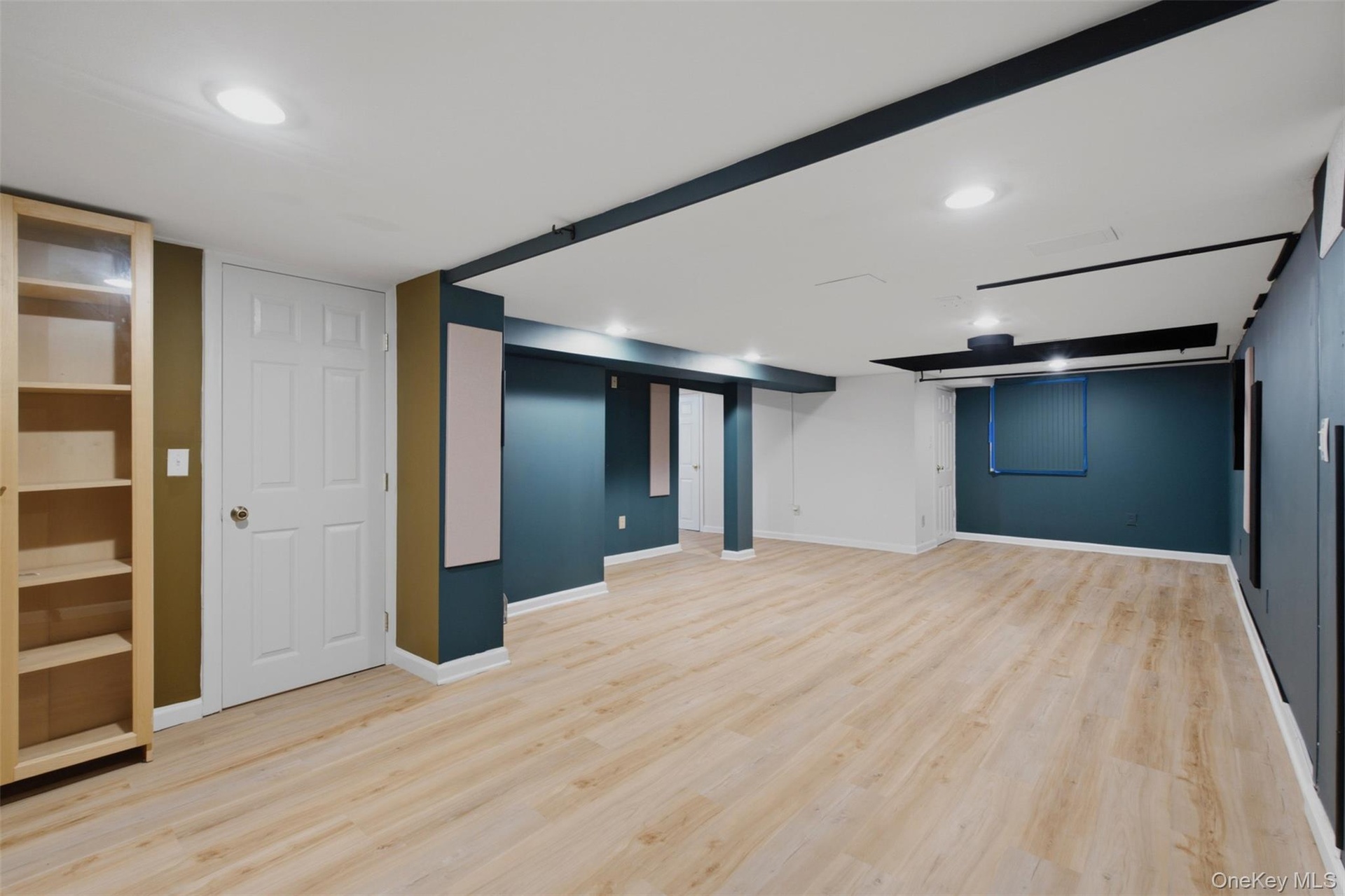 Spacious basement room featuring light wood-finish flooring, recessed lighting, accent walls, built-in shelving, and white trim