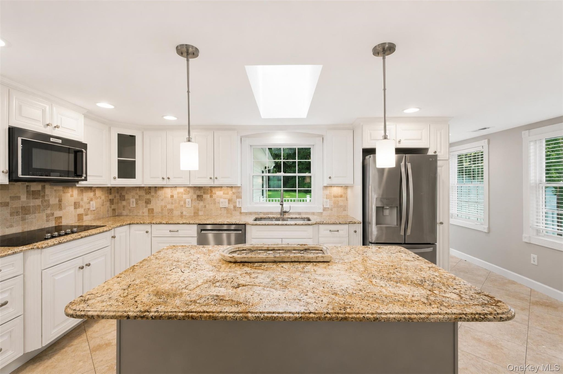 Kitchen featuring a central island with a stone countertop, white cabinetry, integrated stainless steel appliances, a tile backsplash, and recessed li
