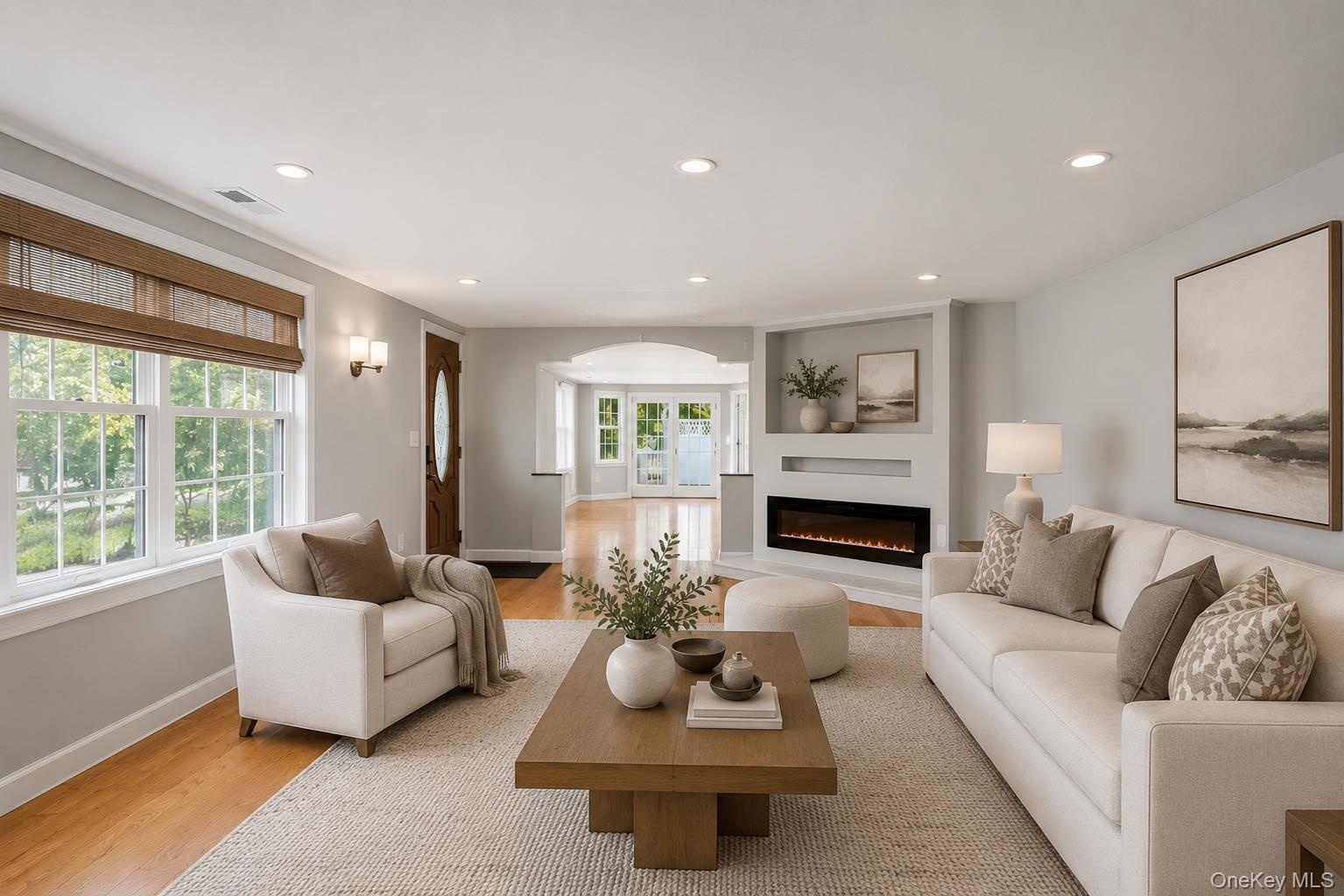 Bright living space featuring wood-finish flooring, recessed lighting, and an integrated electric fireplace with shelving above