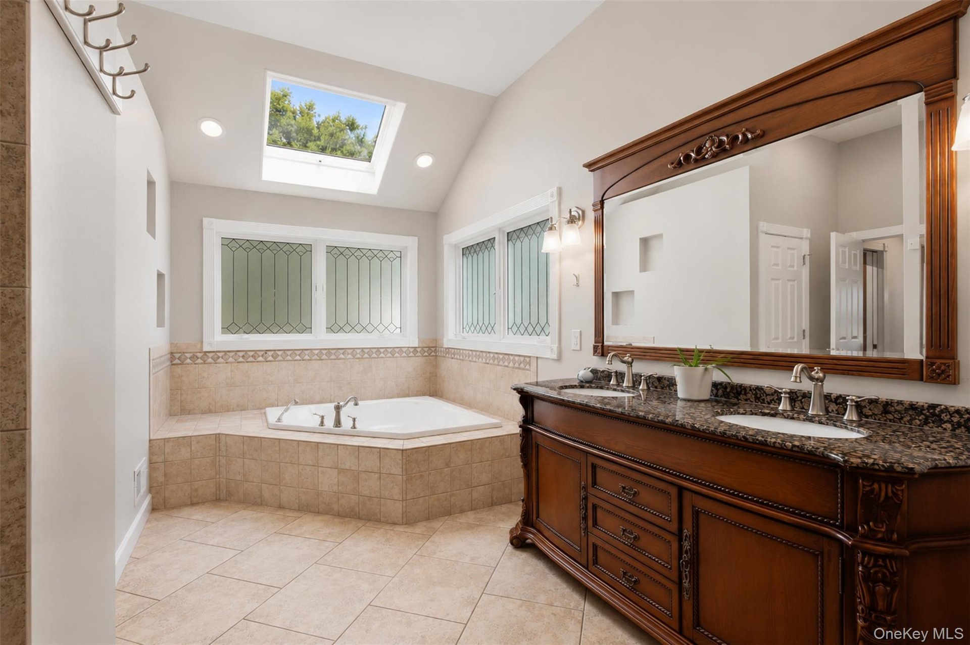 Bathroom featuring a built-in corner jet tub with tiled surround, a large skylight, vaulted ceiling, and recessed lighting