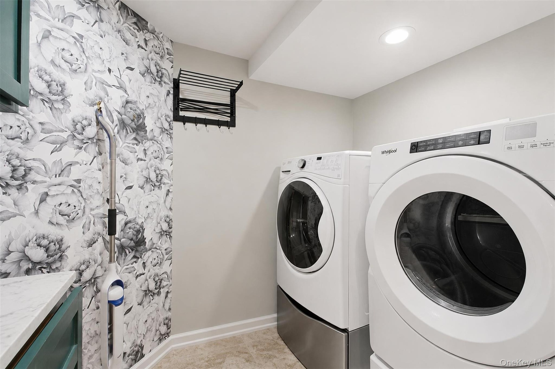 Dedicated laundry area featuring a front-load washer and dryer set on pedestals, recessed lighting, patterned accent wall, and a folding drying rack