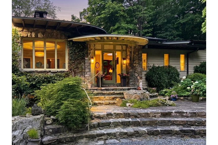Craftsman influenced Mid-Century Modern design features a glass entry, protected by deep eaves, while concentric rings of stone steps through a native