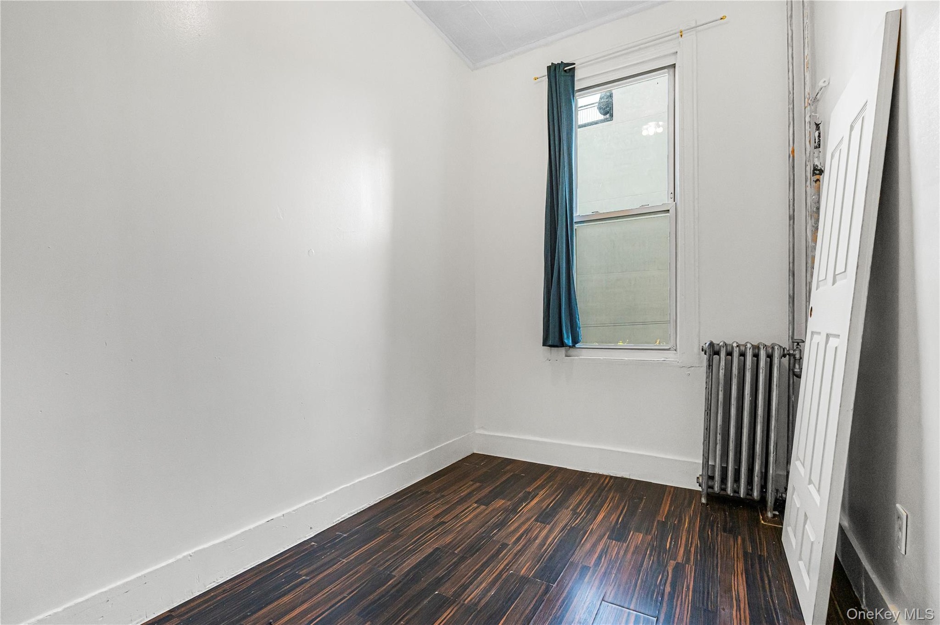 Bright room featuring wood-finish flooring, white walls, and a window with a dark curtain