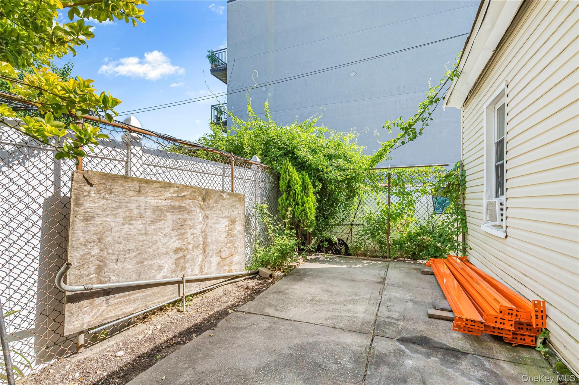 Paved outdoor area with chain-link fencing, mature greenery, and a light-colored siding exterior