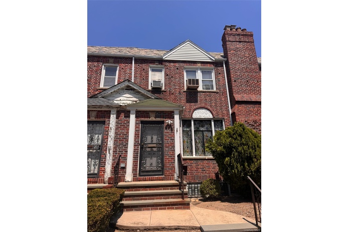 Brick facade featuring a decorative entry door with security screen, stone steps, metal handrails, and a prominent brick chimney