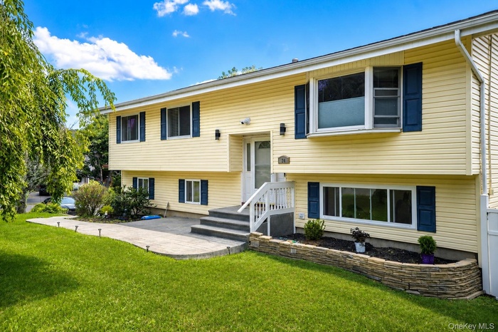 Split-level residence featuring yellow siding, dark blue shutters, and a front entry with a white railing