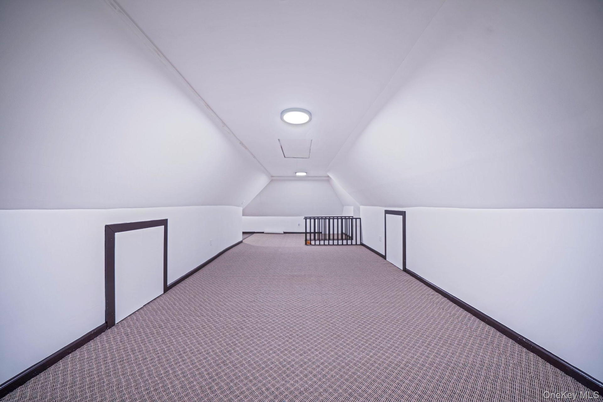 Expansive attic space featuring sloped ceilings, recessed lighting, patterned carpeting, and multiple integrated storage access points