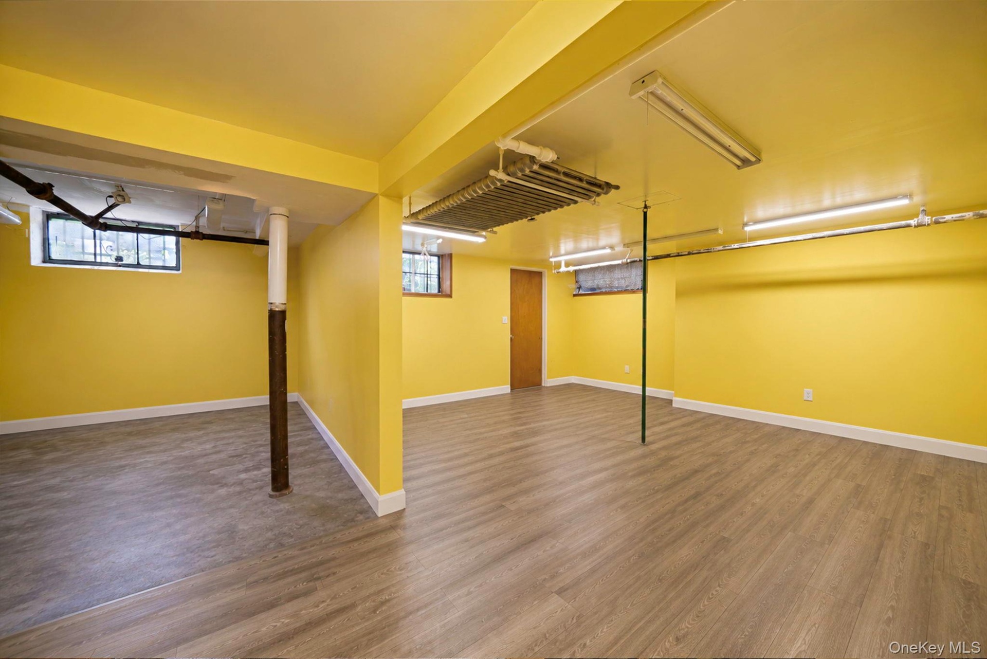 Lower level featuring wood-finish flooring, bright yellow walls, white trim, and multiple fluorescent lighting fixtures