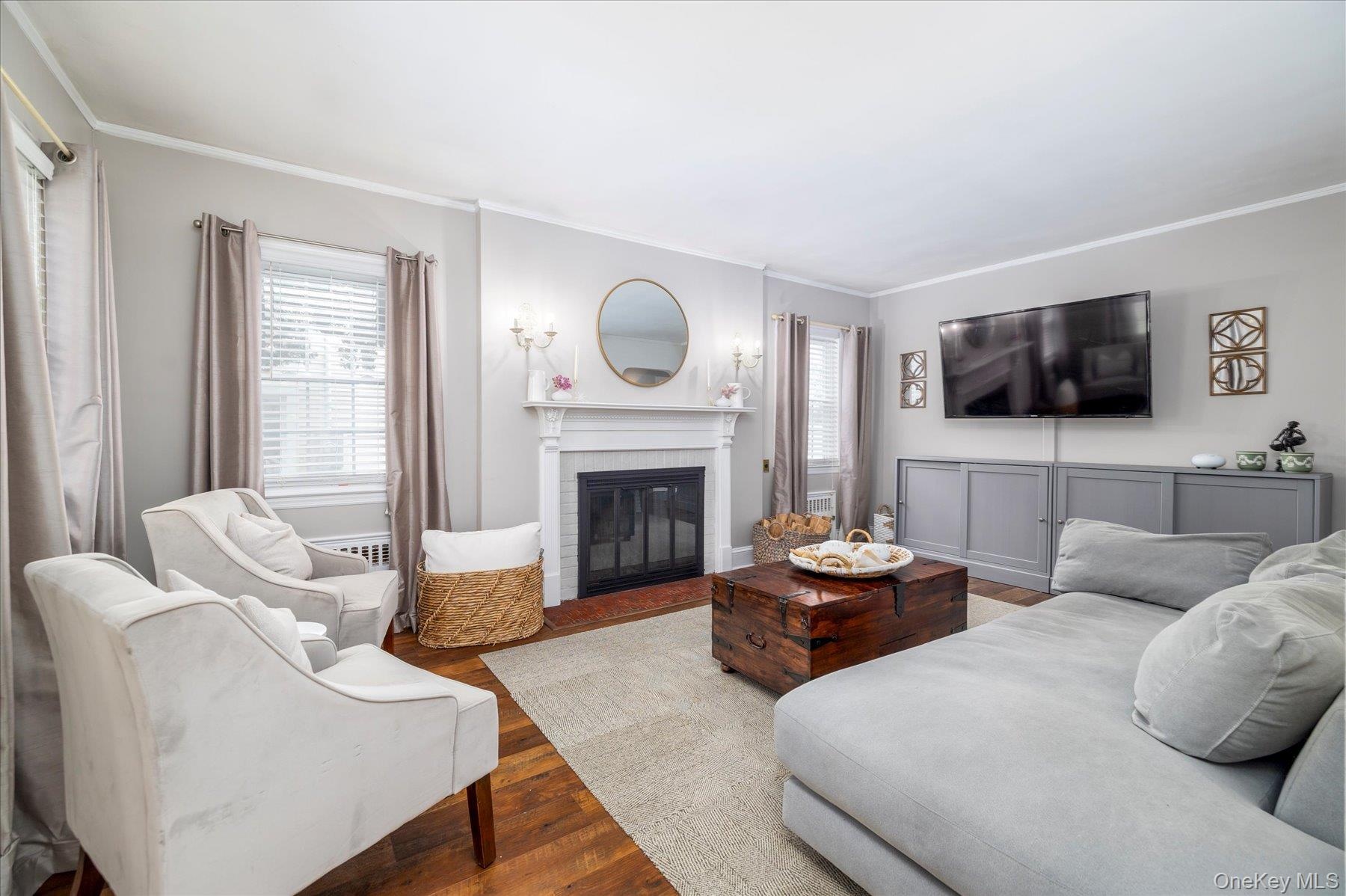 Living room featuring hardwood flooring and a wood burning fireplace with a white mantel and hearth