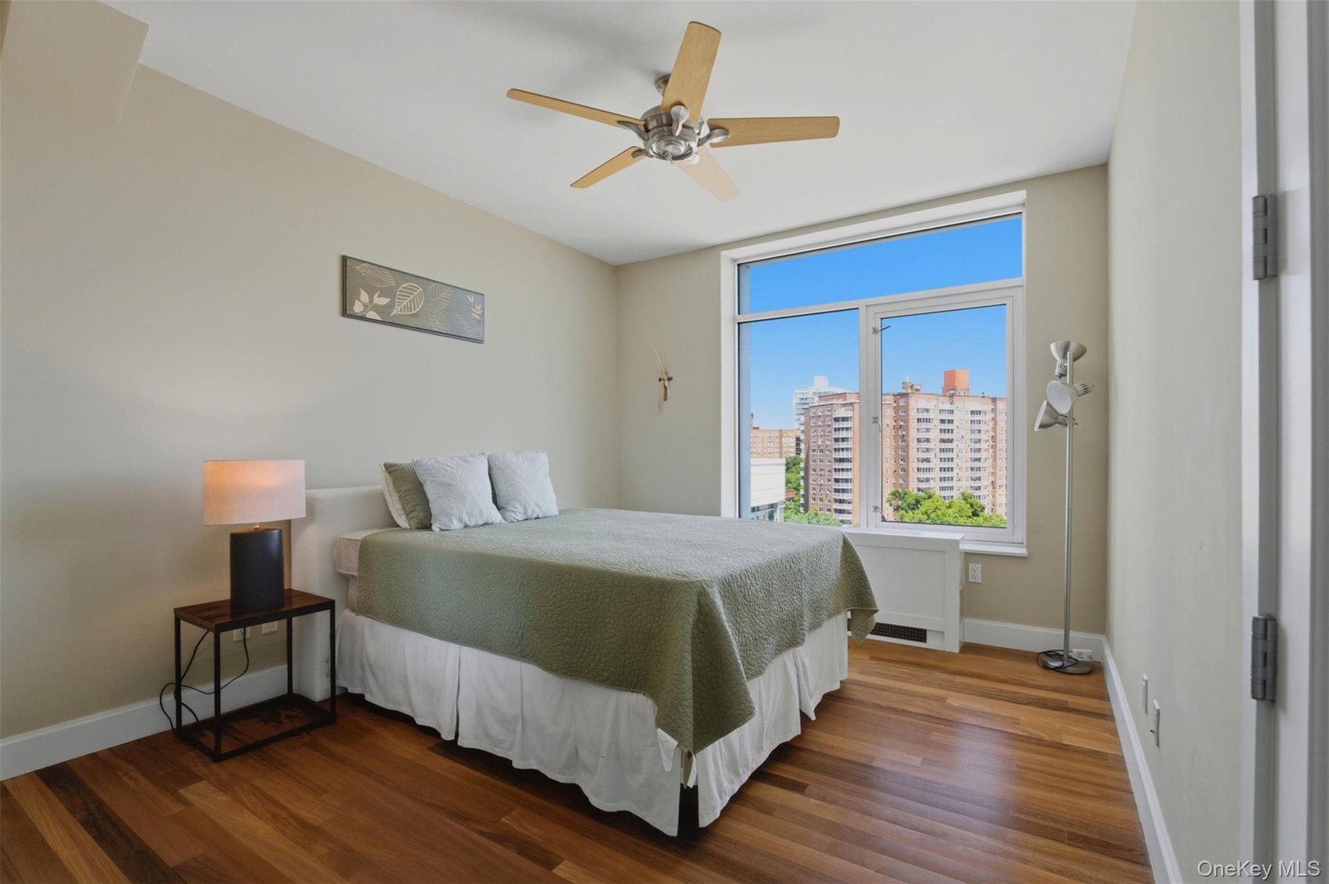 Bedroom 3 featuring wood-finish flooring, a contemporary ceiling fan, and a large window offering urban building views