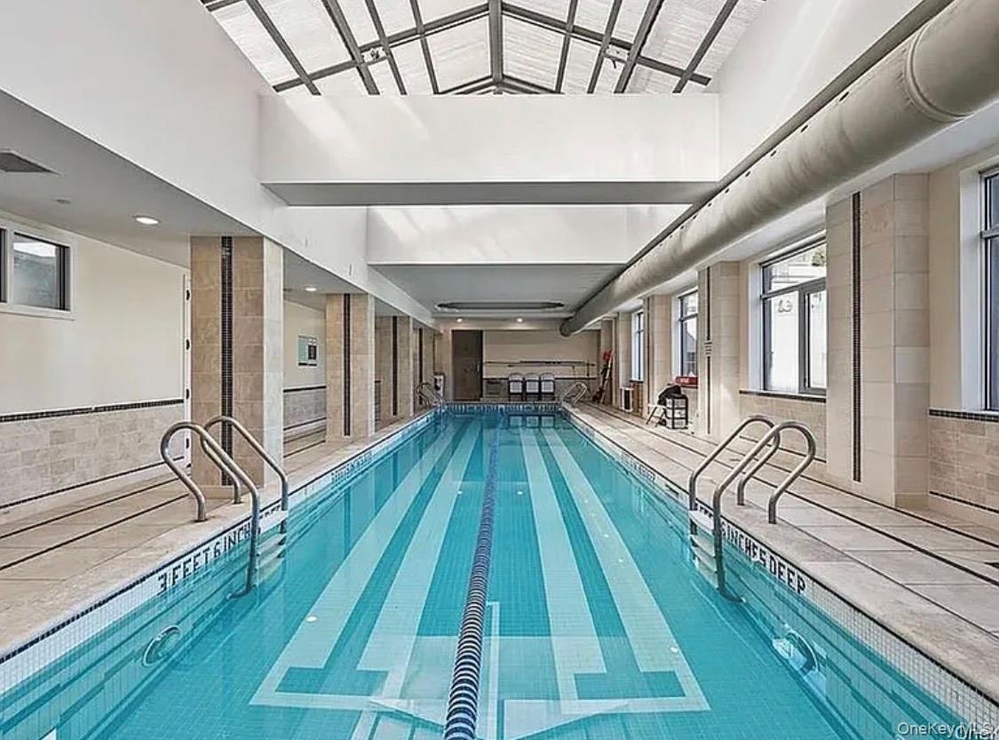 Indoor lap pool with a vaulted glass ceiling, tiled walls, and multiple windows