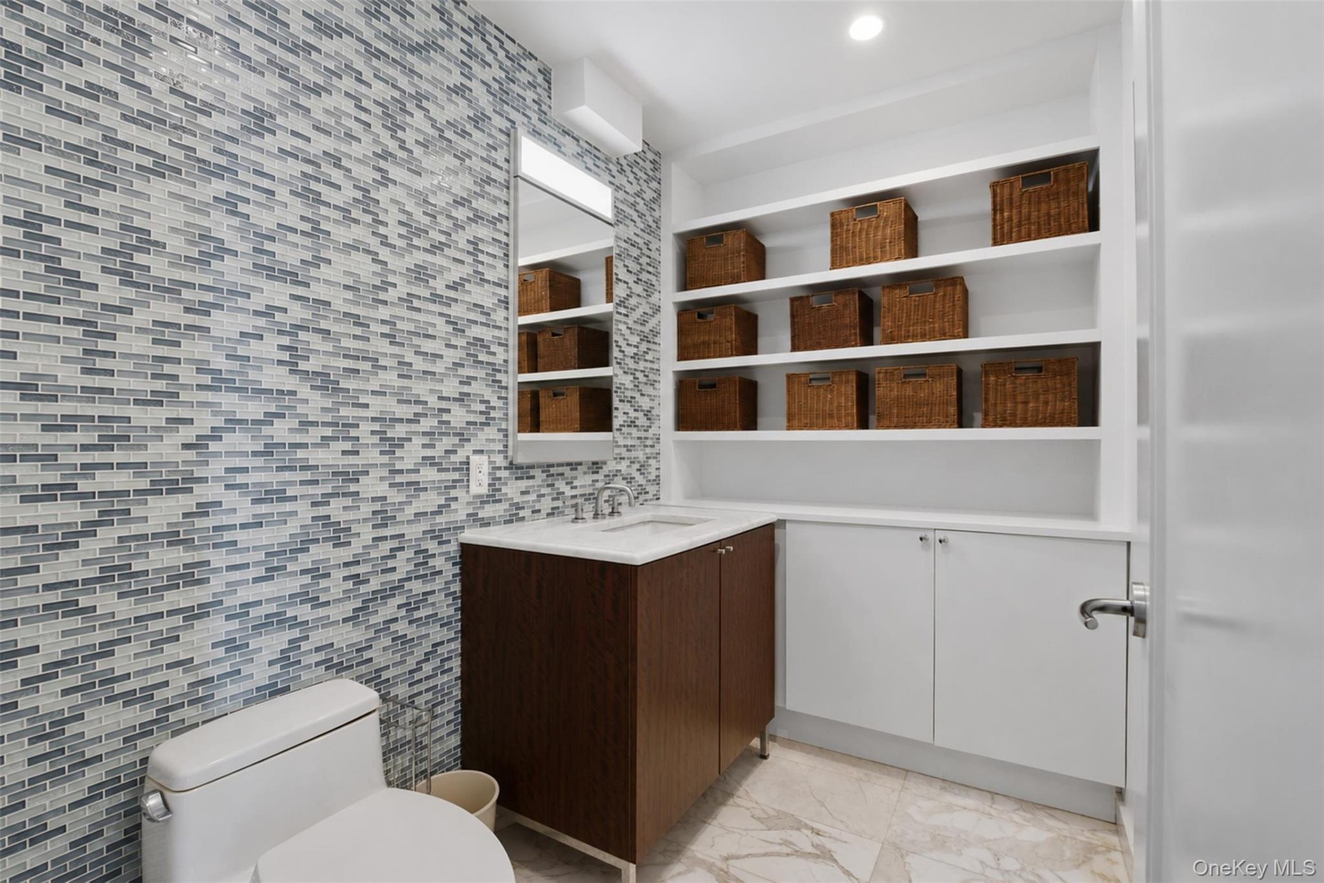 Powder room featuring a full wall of mosaic tile, a wood-finish vanity with a white countertop, and extensive built-in shelving