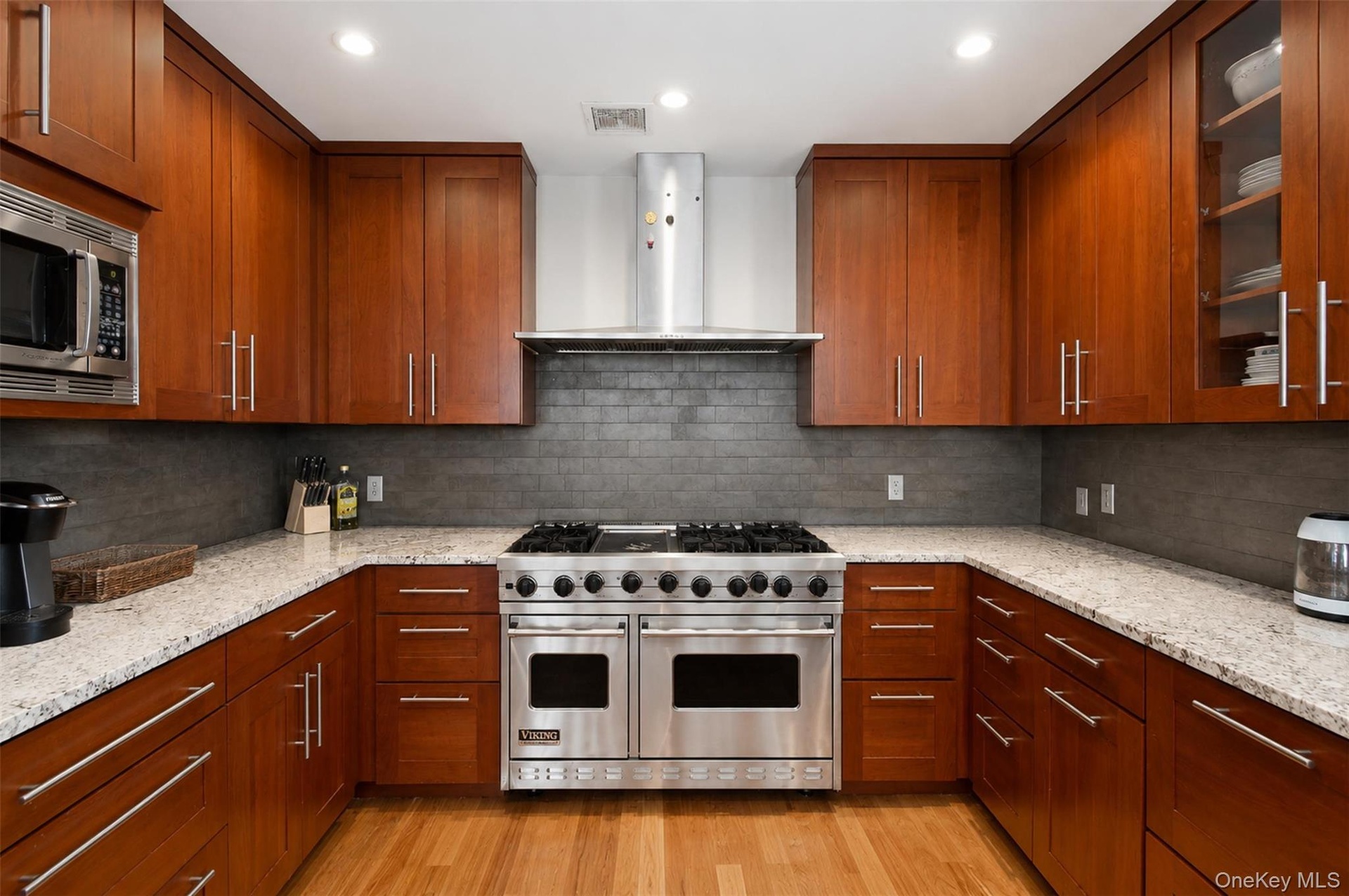 Gourmet kitchen featuring a stainless steel gas range, wood-finish cabinetry, light-toned countertops, tile backsplash, and recessed lighting