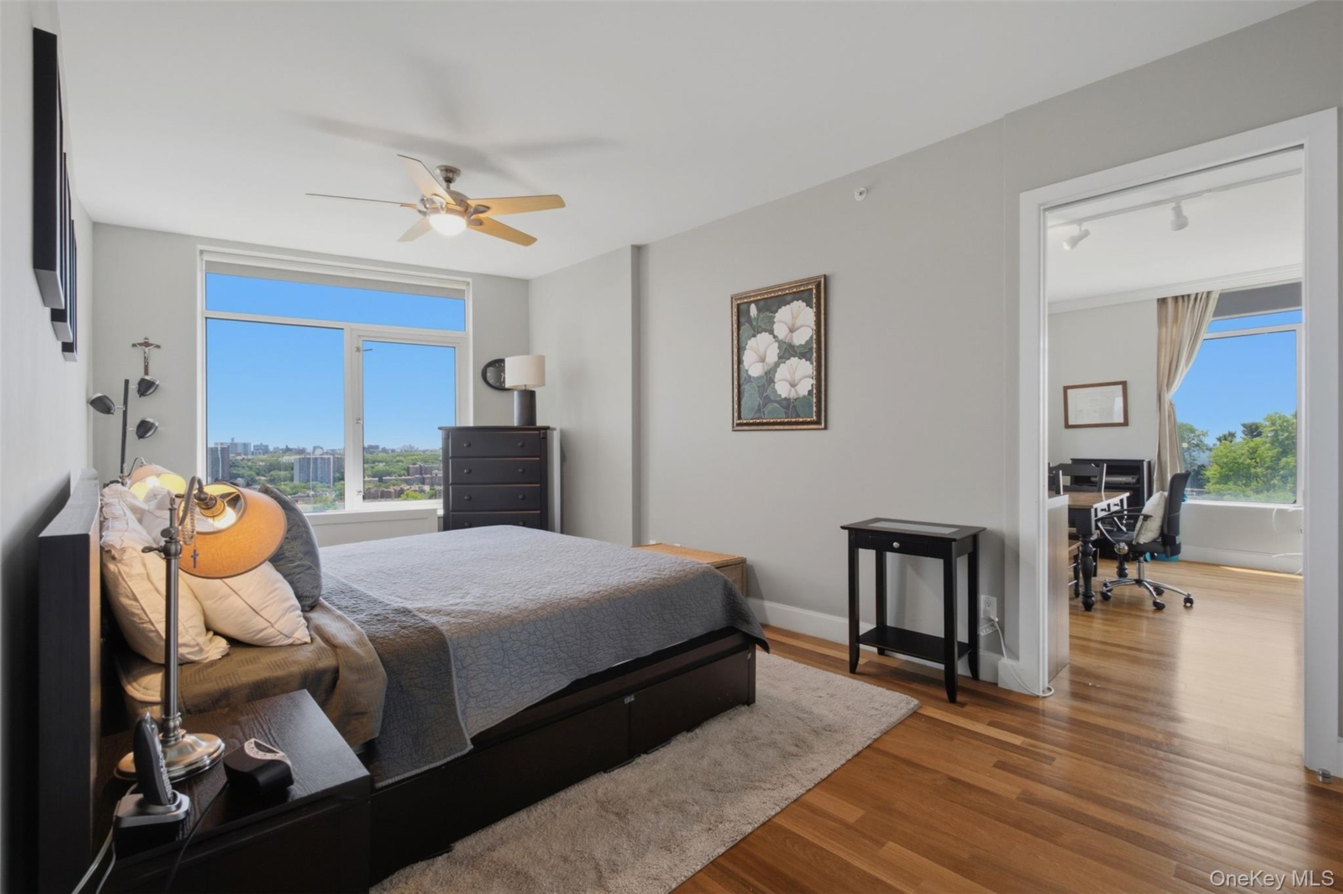 Bedroom 2 featuring a large window with city and tree-lined panoramas, wood-finish flooring, light gray wall paint, and a ceiling fan