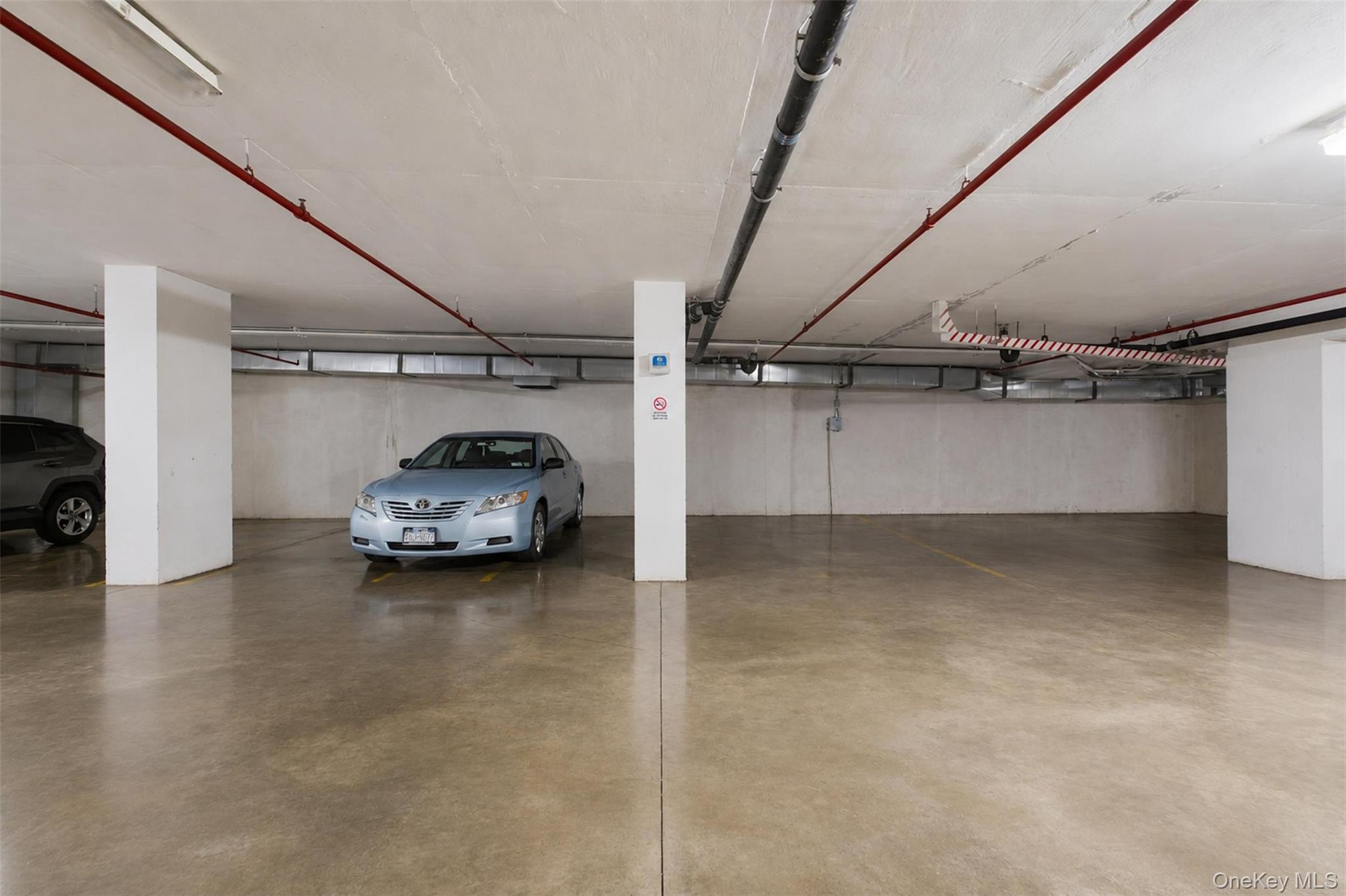 2 Dedicated parking spaces within a subterranean garage, featuring polished concrete flooring and overhead utility lines